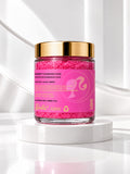 ADAY x Barbie Sugar Body Scrub, a glass jar of hot-pink scrub with a gold lid on a white pedestal