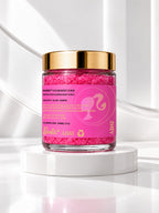 ADAY x Barbie Sugar Body Scrub, a glass jar of hot-pink scrub with a gold lid on a white pedestal