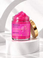 An open jar of ADAY x Barbie Sugar Body Scrub with its gold lid alongside