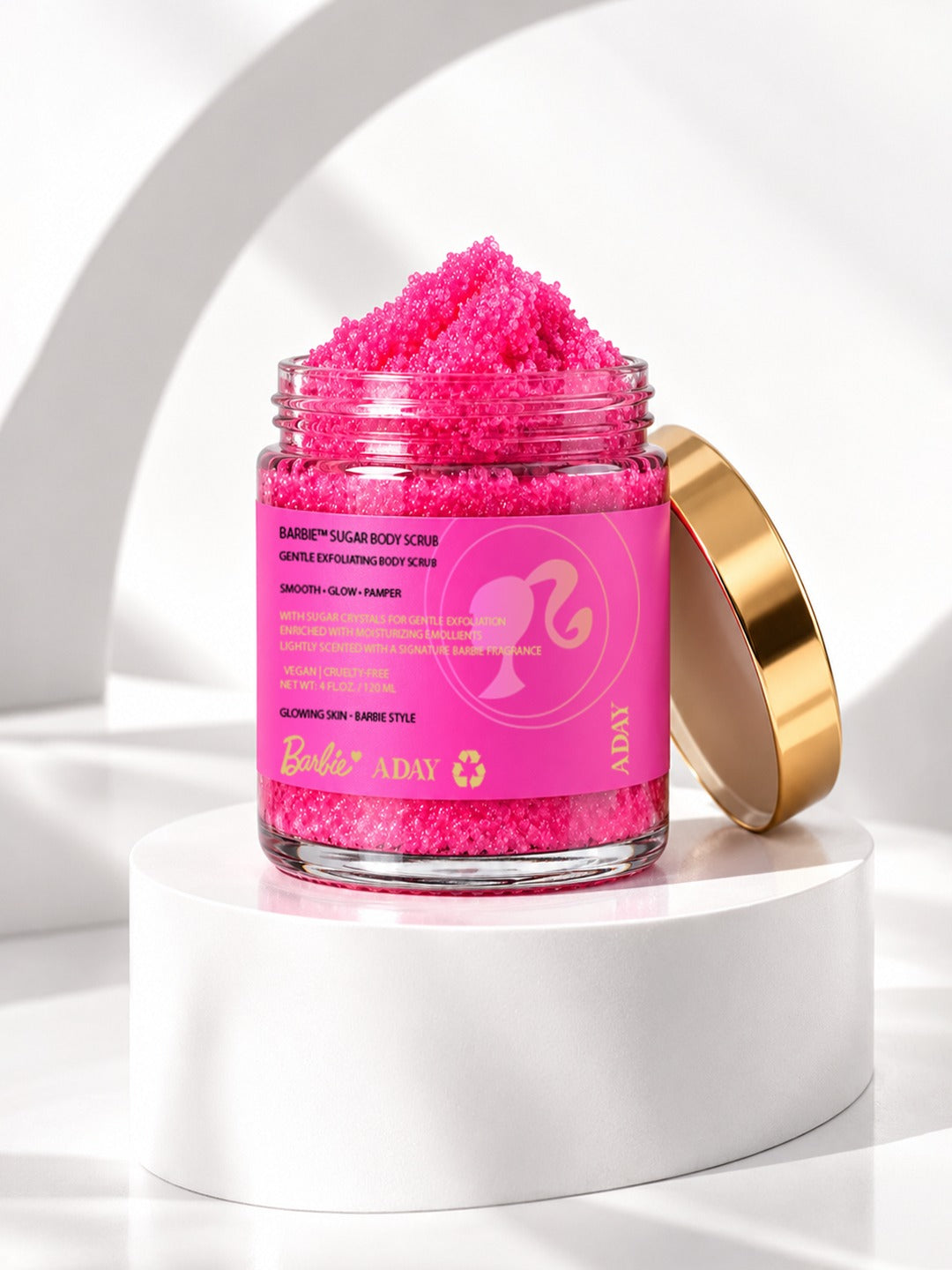 An open jar of ADAY x Barbie Sugar Body Scrub with its gold lid alongside