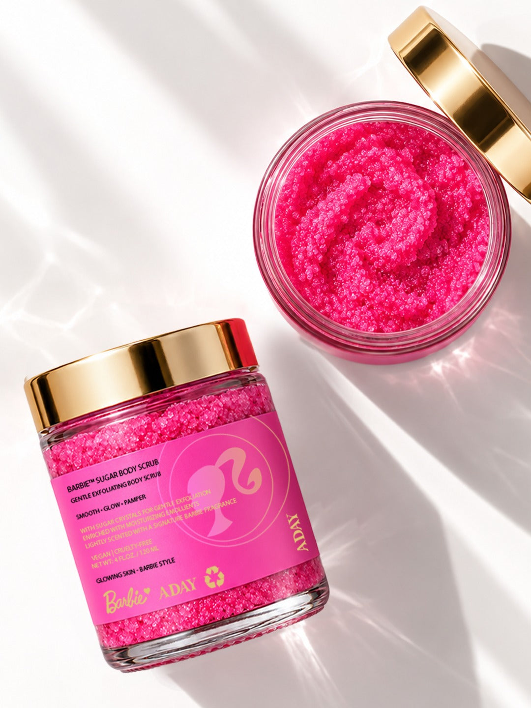 An open jar of ADAY x Barbie Sugar Body Scrub seen from above beside a closed jar