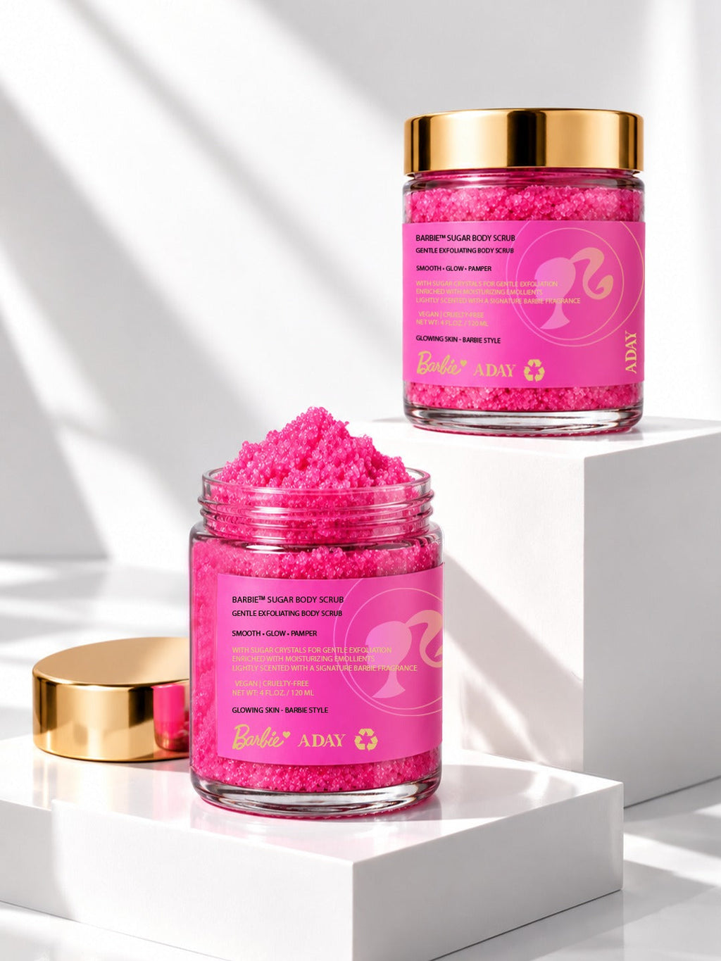 Two jars of ADAY x Barbie Sugar Body Scrub on white plinths, one open
