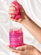 A hand lifting a scoop of ADAY x Barbie Sugar Body Scrub above the open jar