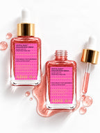 Two bottles of ADAY Crystal Rush Shimmer Body Serum beside the dropper and a spill of pink shimmer serum