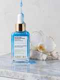ADAY Electric Aura Shimmer Body Serum, a 50 ml blue glass dropper bottle on marble beside a white orchid