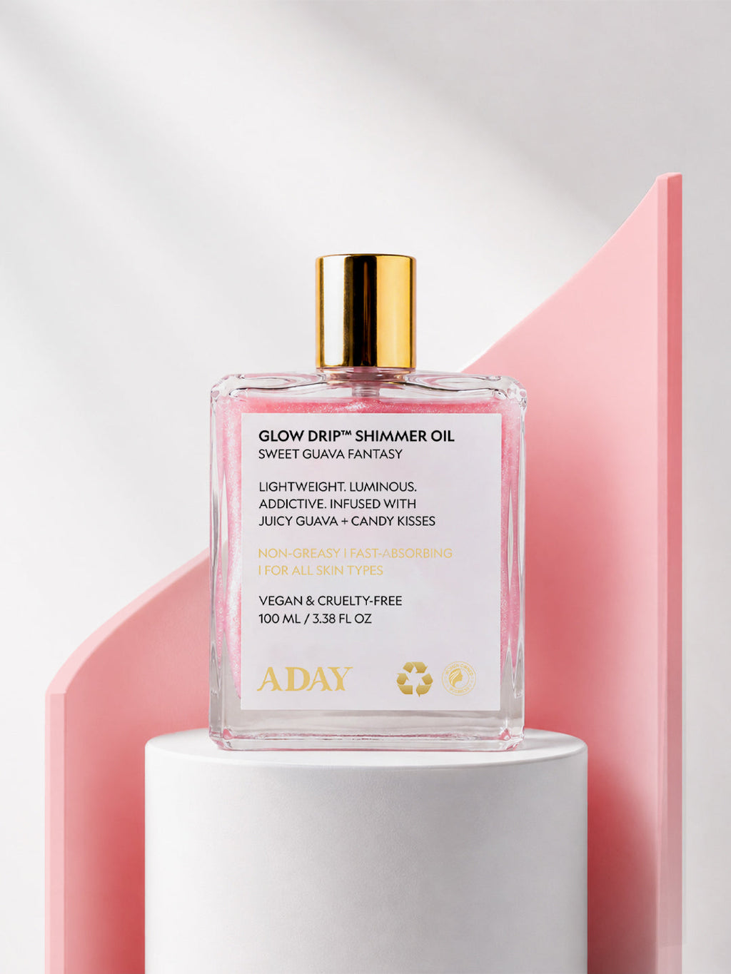 ADAY Glow Drip Shimmer Oil in Sweet Guava Fantasy, a 100 ml gold-capped glass bottle on a white pedestal