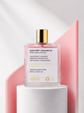 ADAY Glow Drip Shimmer Oil in Sweet Guava Fantasy, a 100 ml gold-capped glass bottle on a white pedestal