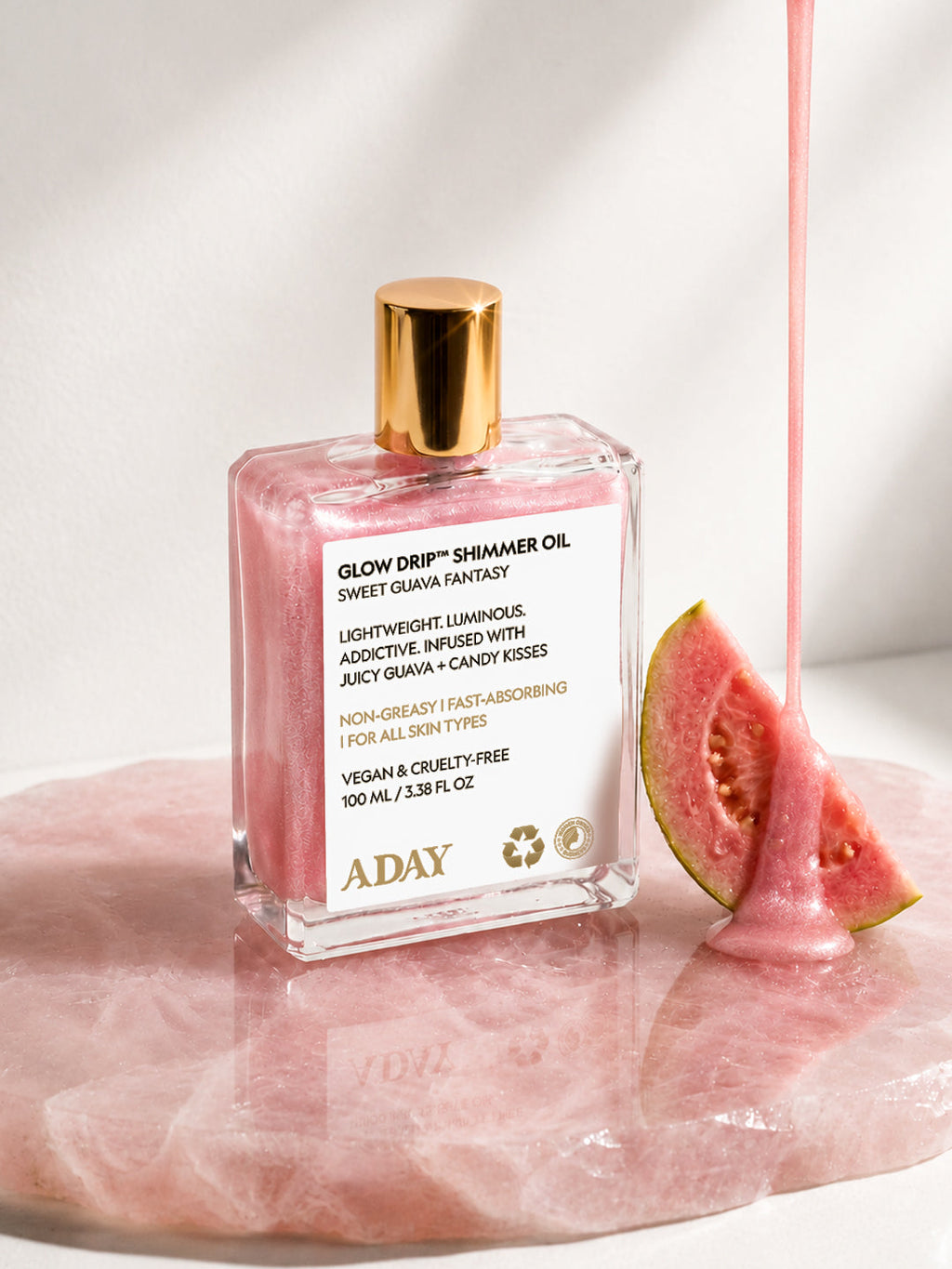 ADAY Glow Drip Shimmer Oil resting on blush silk beside a wedge of fresh guava