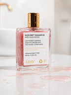 ADAY Glow Drip Shimmer Oil standing in a pool of spilled pink shimmer oil