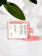 ADAY Glow Drip Shimmer Oil on its side with pink oil pouring from the neck, green leaves behind