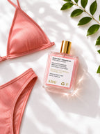 ADAY Glow Drip Shimmer Oil in a flatlay with coral swimwear and green leaves