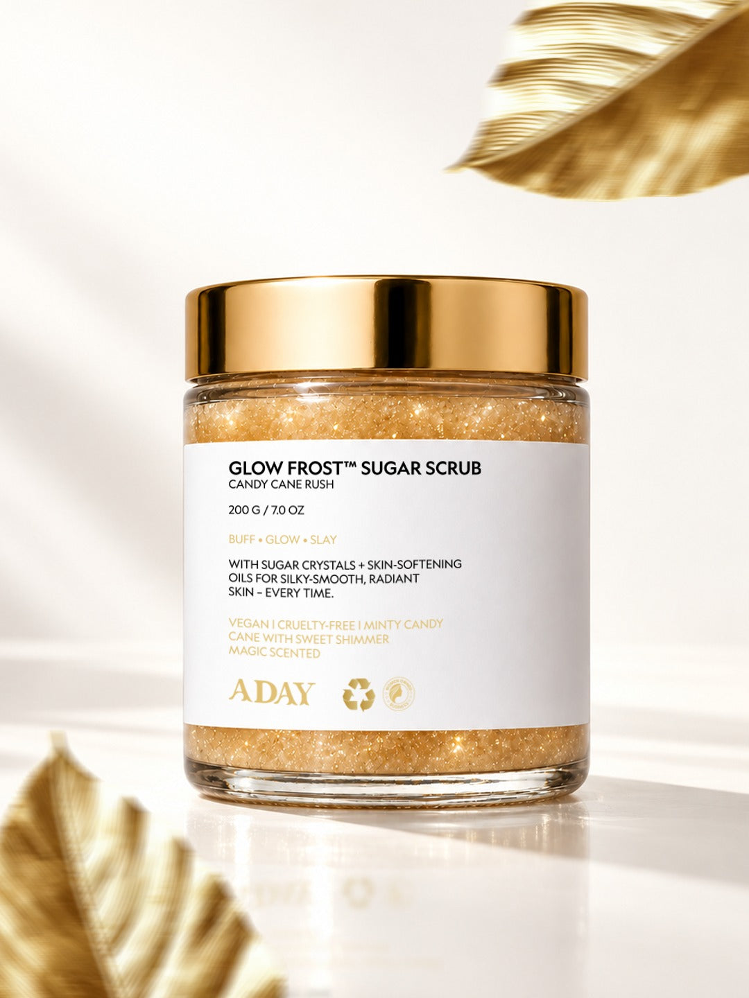 A closed jar of ADAY Glow Frost Sugar Scrub with gilded palm leaves on cream silk