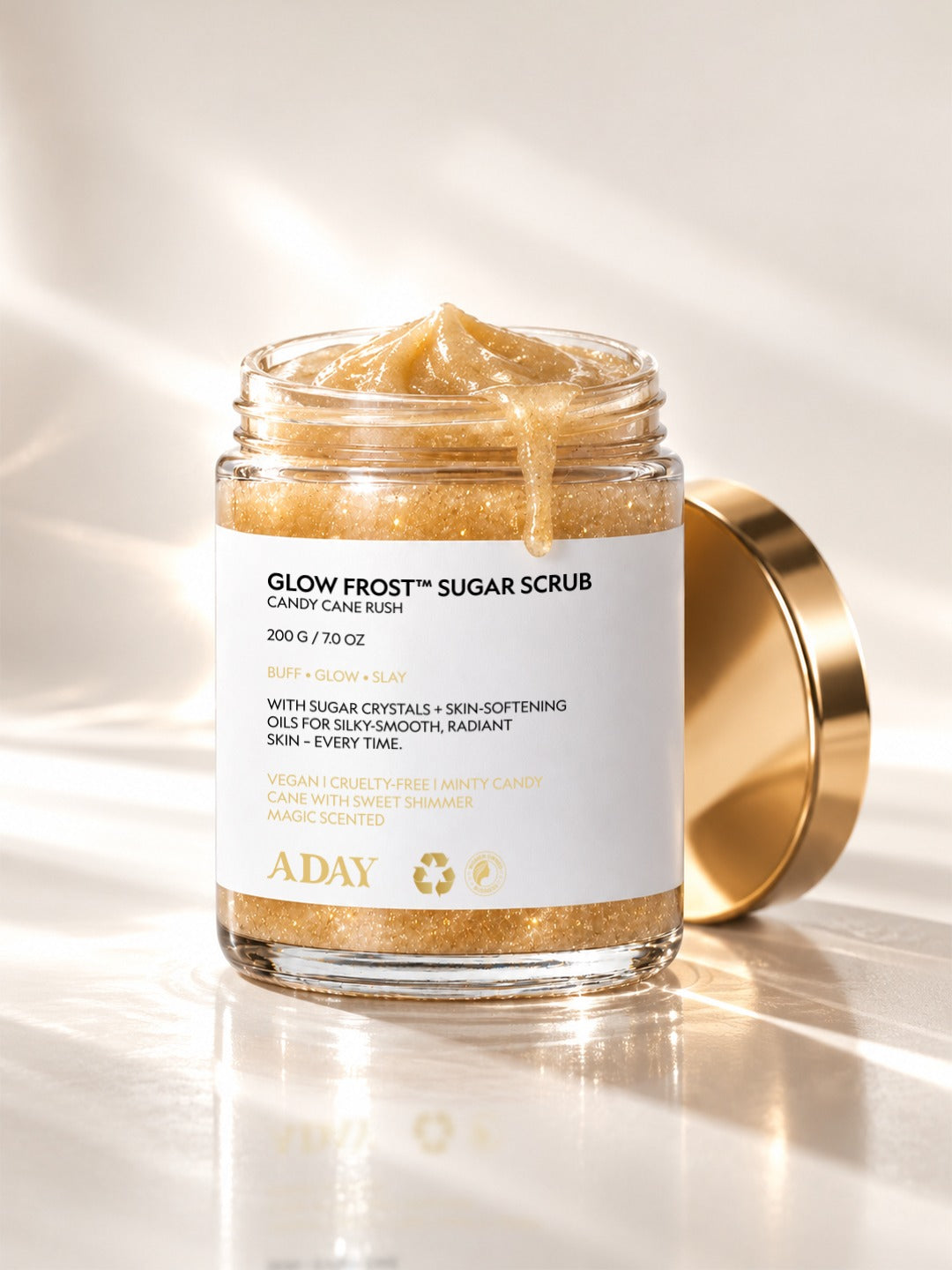 An open jar of ADAY Glow Frost Sugar Scrub, gold lid set to one side