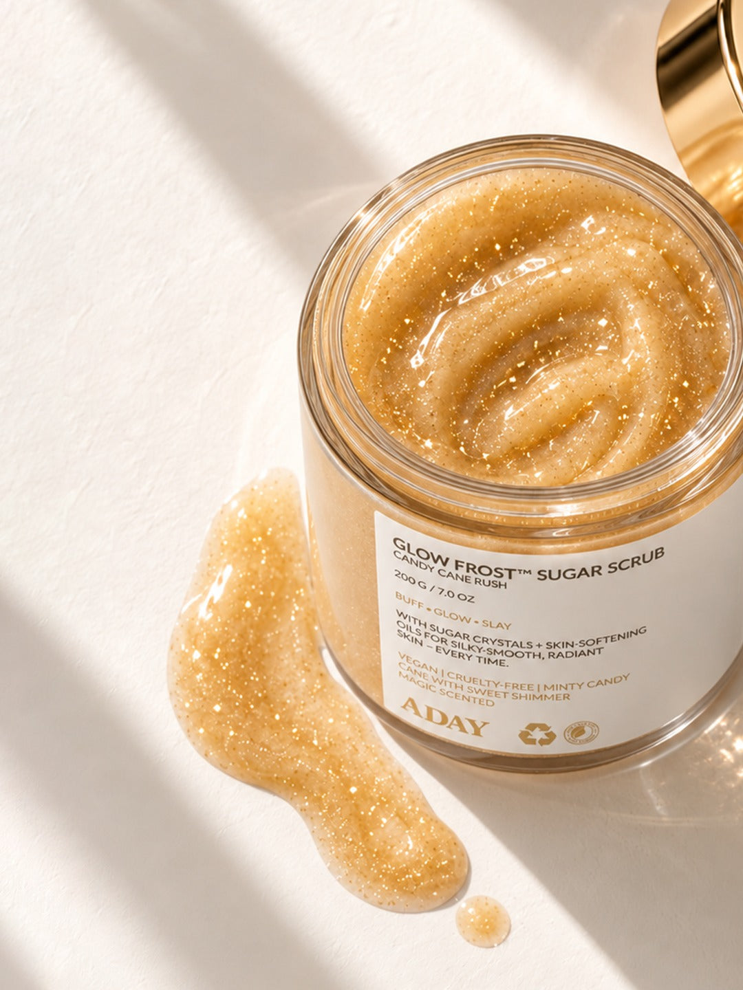An open jar of ADAY Glow Frost Sugar Scrub with the golden scrub spilling out