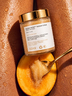 A gold spoon lifting ADAY Glow Frost Sugar Scrub from the jar against sunlit skin