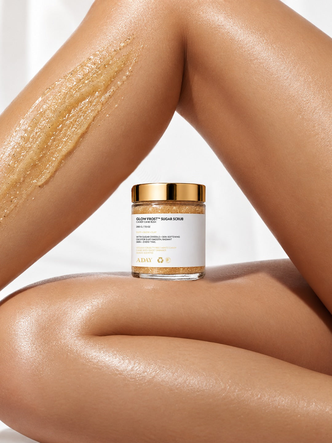 ADAY Glow Frost Sugar Scrub with a swatch of golden scrub on a model's leg