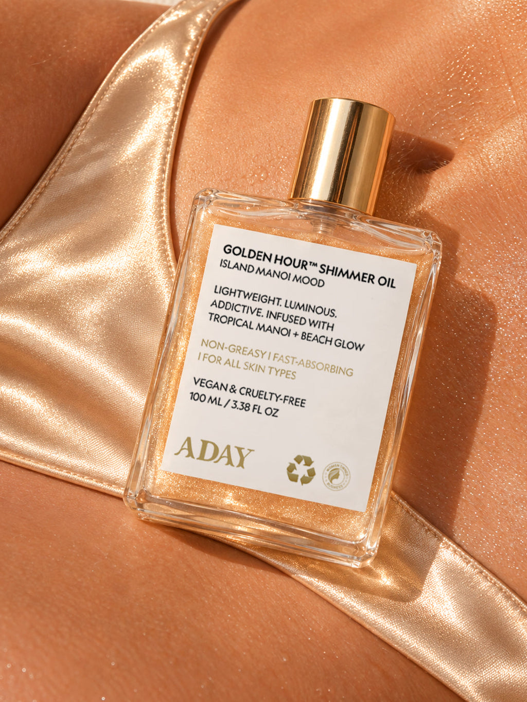 ADAY Golden Hour Shimmer Oil resting on gold satin against shimmering skin