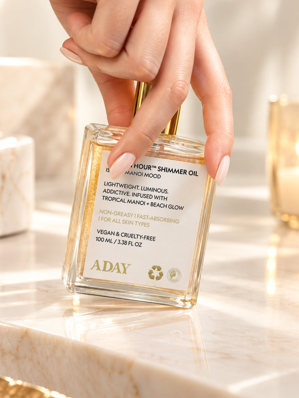 A hand reaching for the ADAY Golden Hour Shimmer Oil on a marble vanity