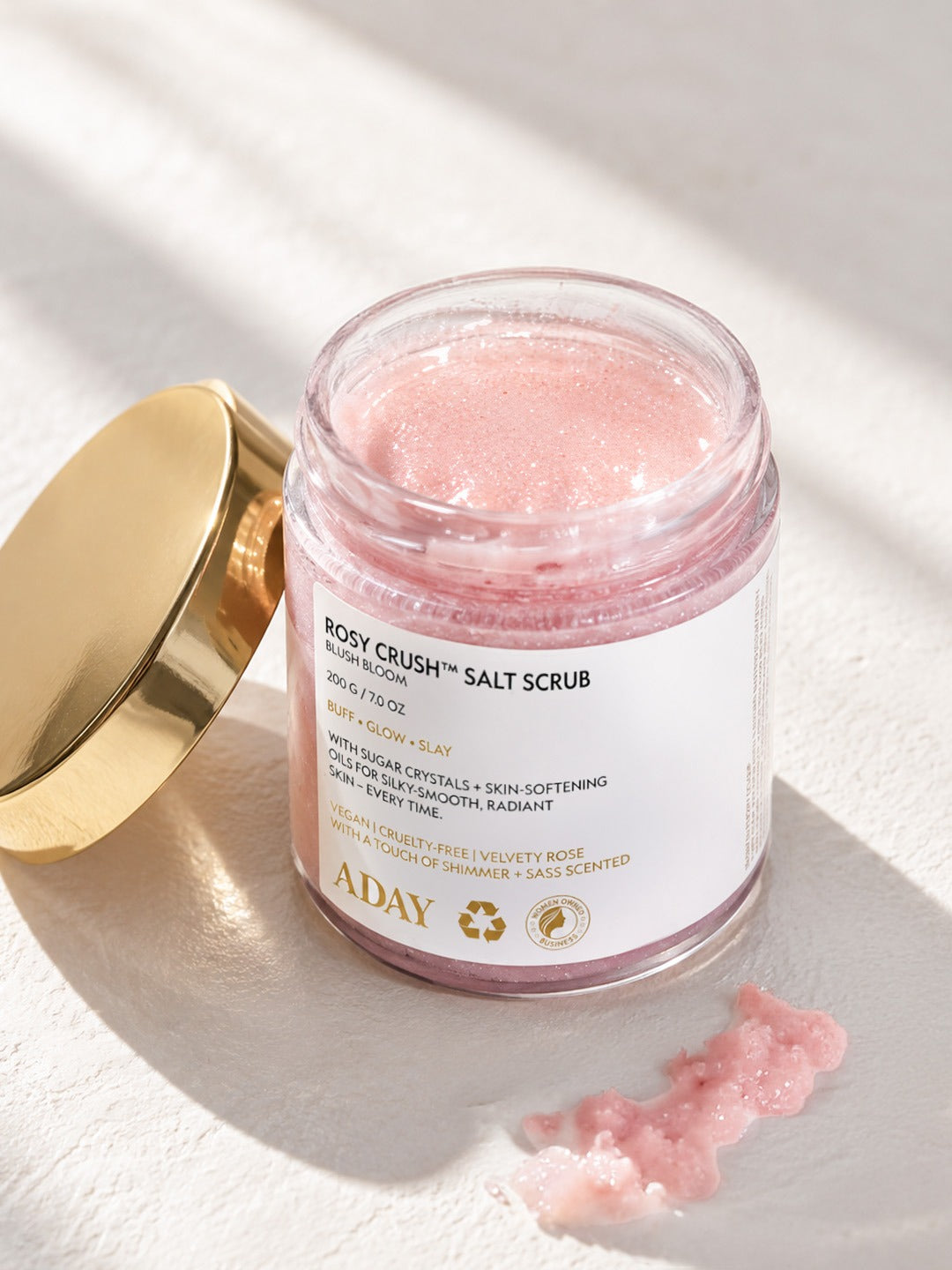 An open jar of ADAY Rosy Crush Salt Scrub with its gold lid resting alongside