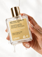 A hand holding the ADAY Soft Halo Shimmer Oil with oil dripping from the bottle