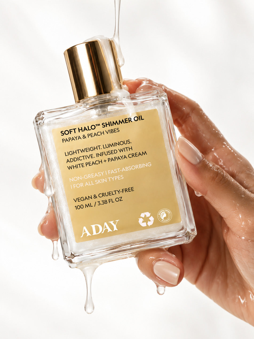 A hand holding the ADAY Soft Halo Shimmer Oil with oil dripping from the bottle
