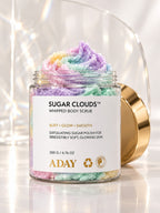 Open jar of ADAY Sugar Clouds Whipped Body Scrub with its pastel rainbow swirl peak, gold lid leaning against it