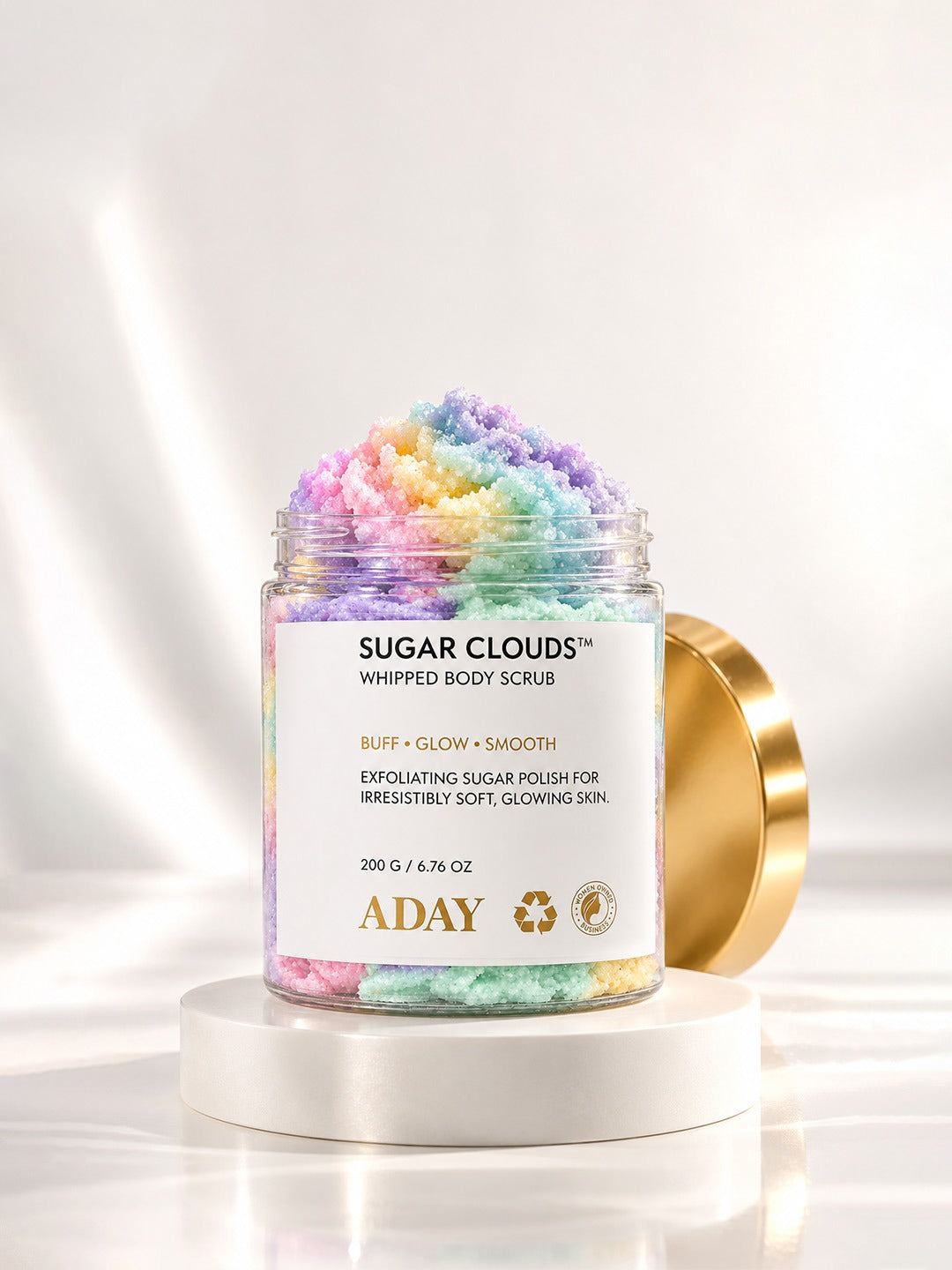ADAY Sugar Clouds Whipped Body Scrub open on a white pedestal, showing the swirled sugar polish