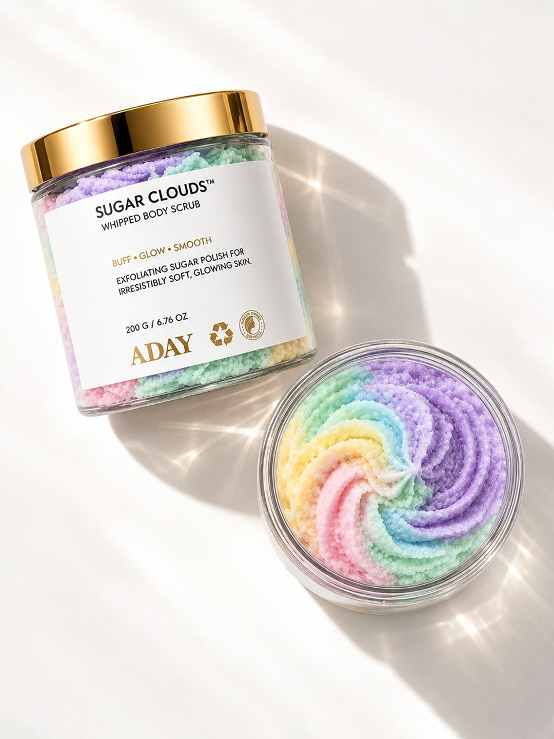ADAY Sugar Clouds Whipped Body Scrub beside a dish of the rainbow-swirled sugar polish