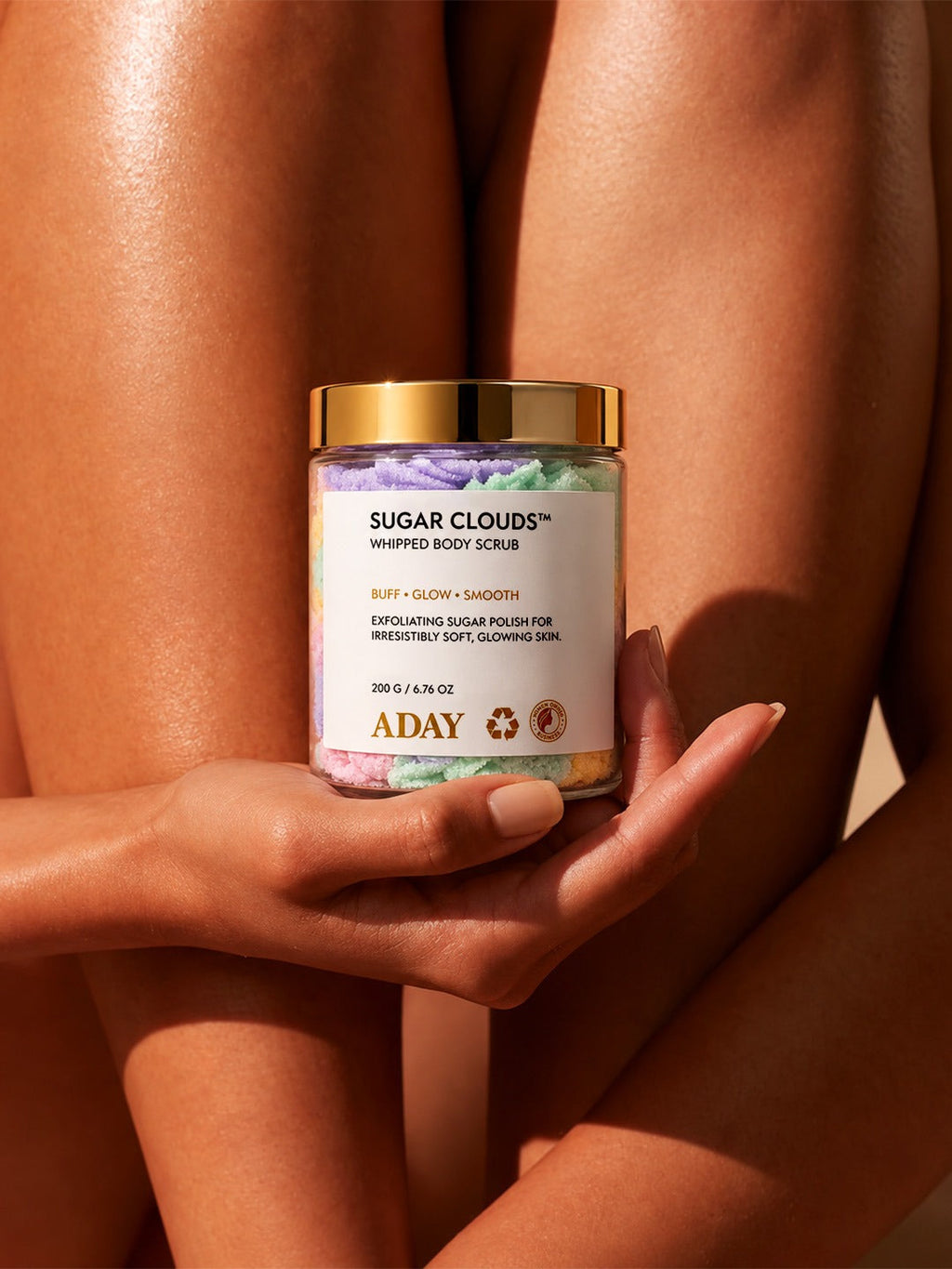 A model holding the ADAY Sugar Clouds Whipped Body Scrub against her legs