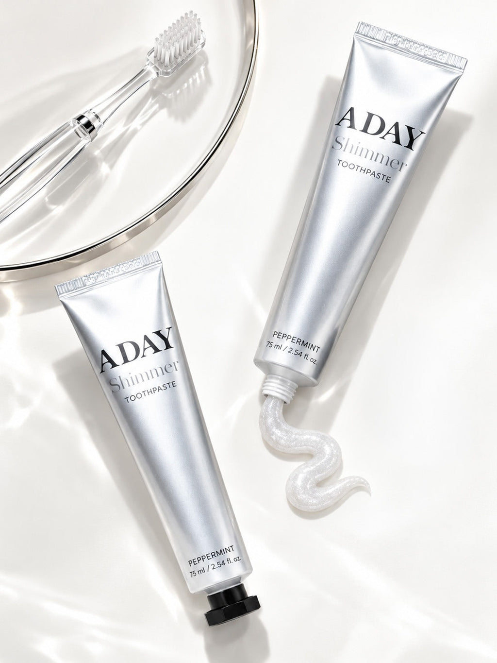 Two tubes of ADAY Silver Shimmer Toothpaste with a toothbrush and a swirl of paste