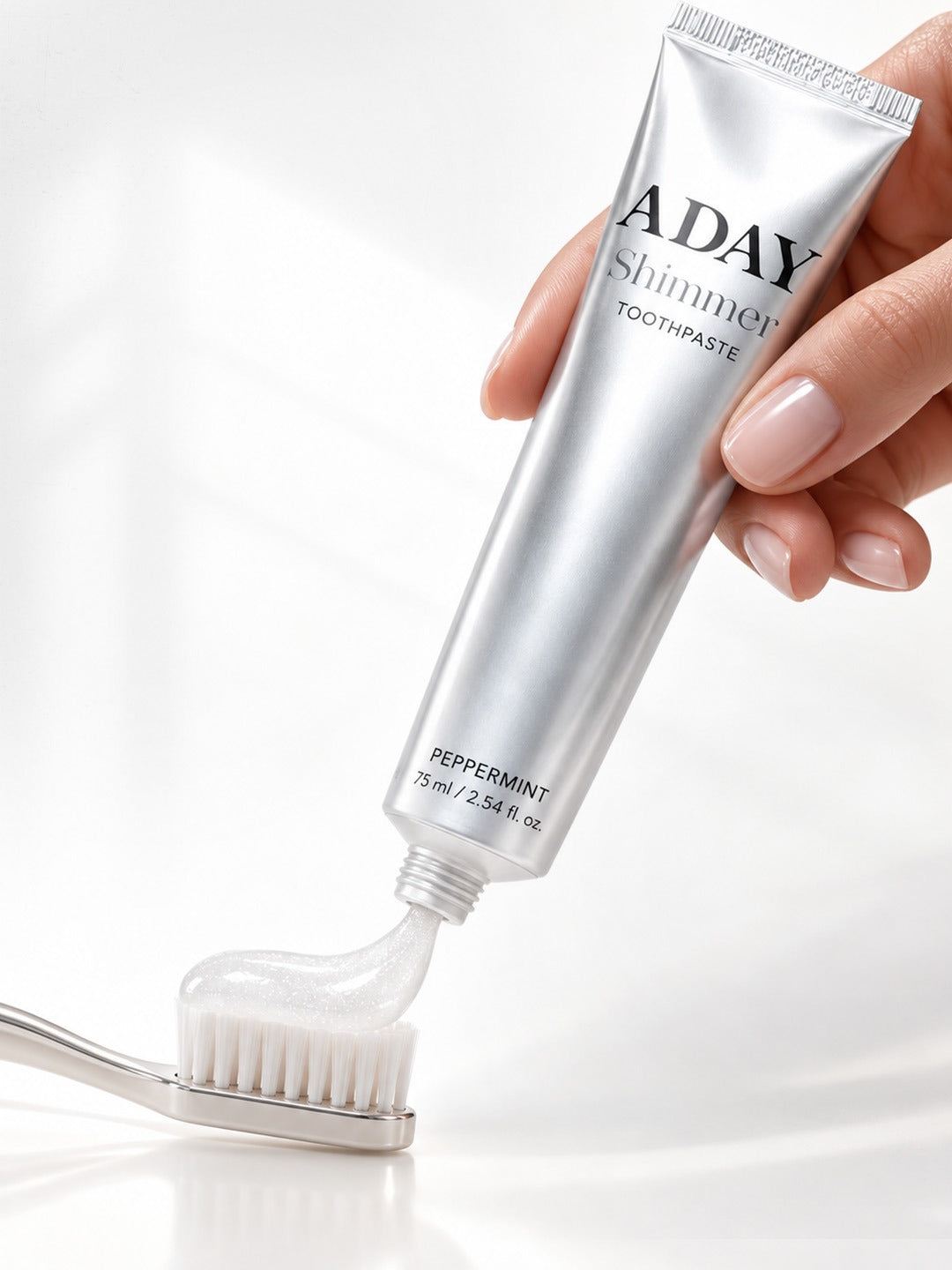 A hand squeezing ADAY Silver Shimmer Toothpaste onto a toothbrush