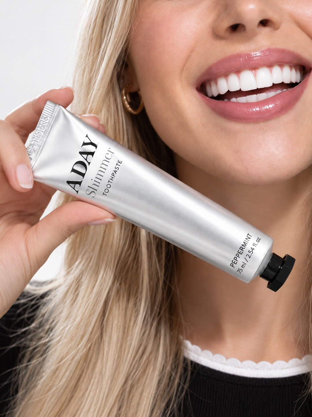 A model holding the ADAY Silver Shimmer Toothpaste beside her smile